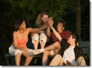 Four students laugh and high-five while sitting on a bench